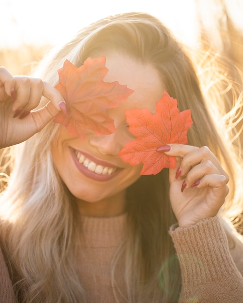 Foto grátis mulher jovem feliz segurando maple folhas e cobrir os olhos ao ar livre