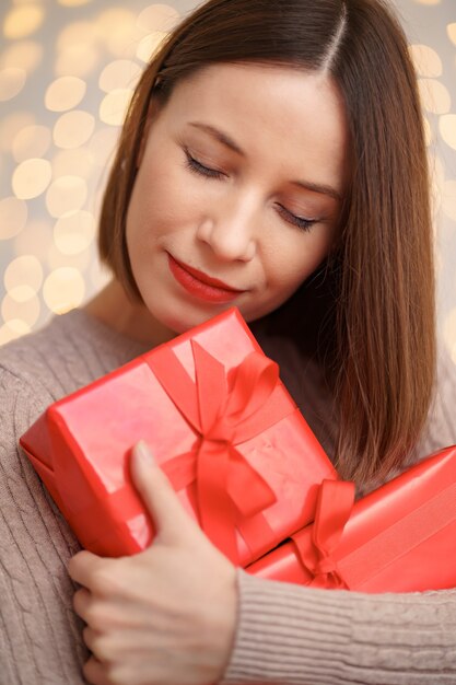 Mulher jovem feliz segurando muitas caixas de presentes com luzes