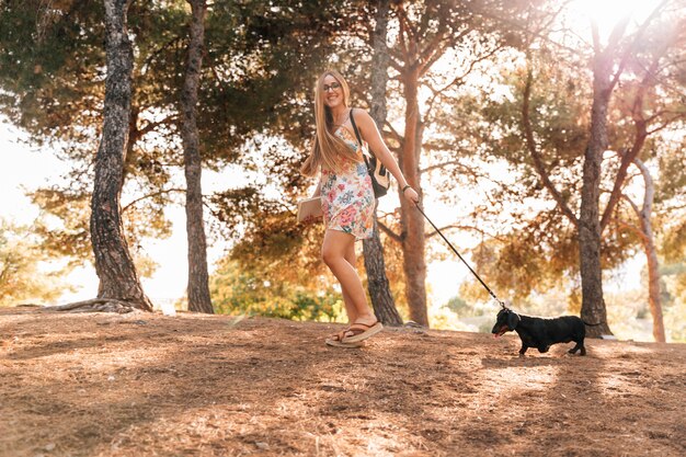 Mulher jovem feliz, segurando o livro andando com seu cachorro no jardim