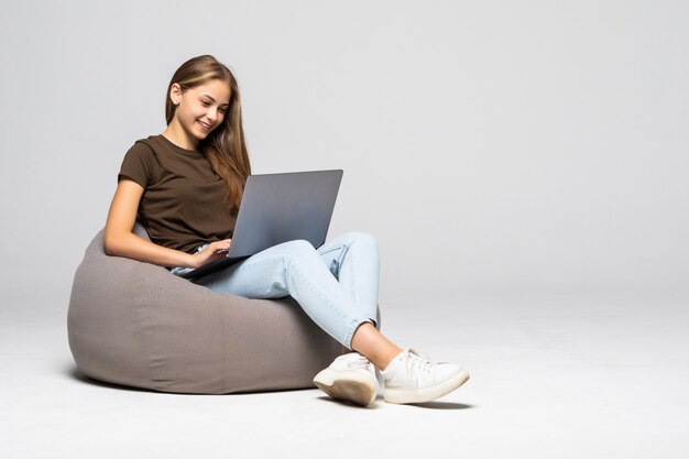 Mulher jovem feliz sentada no chão usando o laptop na parede cinza