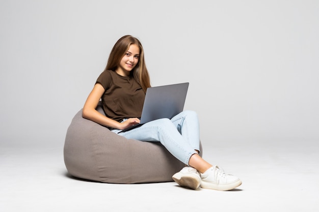 Mulher jovem feliz sentada no chão usando o laptop na parede cinza