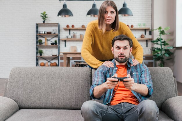 Mulher jovem, ficar, atrás de, dela, marido, sentar sofá, jogando videogame