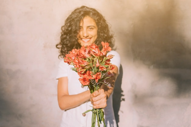 Foto grátis mulher jovem, ficar, contra, parede, segurando, alstroemeria, buquê vermelho flor, em, mãos