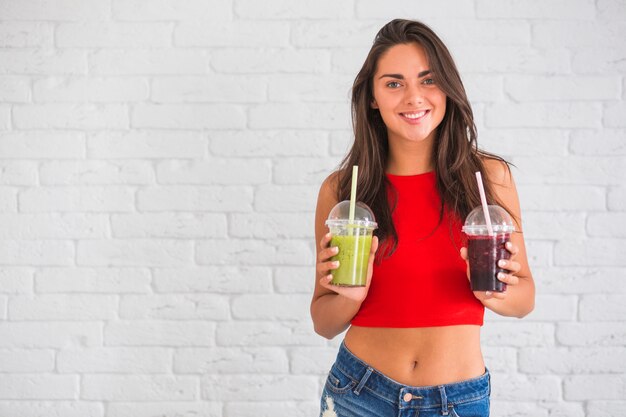 Mulher jovem, ficar, contra, parede, segurando, smoothies, em, copo plástico