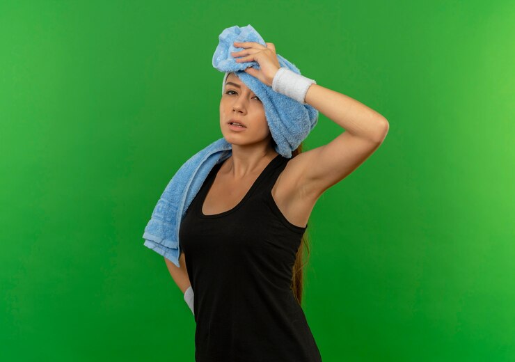Foto grátis mulher jovem fitness em roupas esportivas com fita para a cabeça e uma toalha no pescoço, parecendo cansada e exausta em pé sobre a parede verde