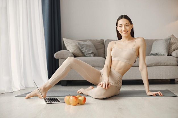 Mulher jovem fitness sentada no tapete de ioga em casa e usando um laptop