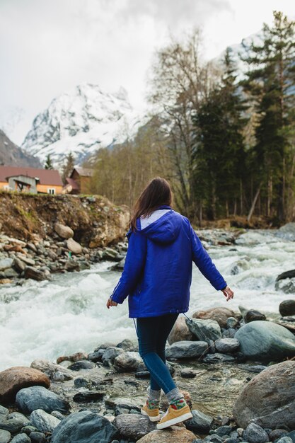 Mulher jovem hippie caminhando sobre uma rocha em um rio na floresta de inverno