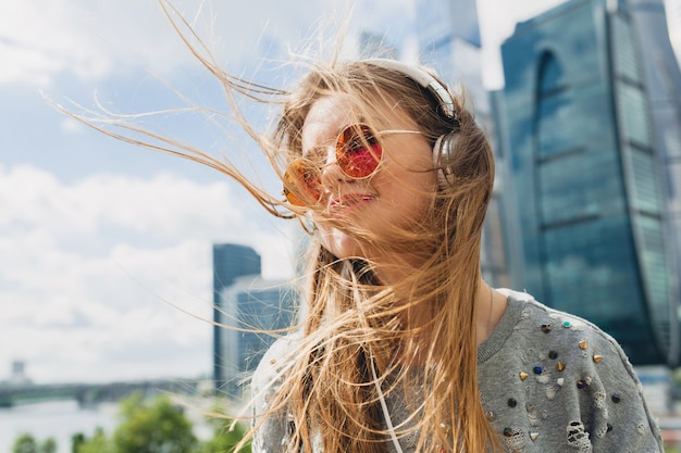 Mulher jovem hippie se divertindo na rua ouvindo música em fones de ouvido, usando óculos de sol rosa