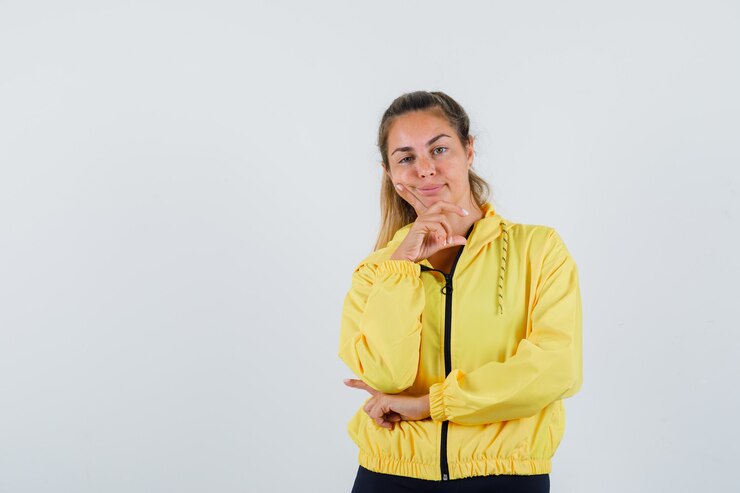 Foto grátis mulher jovem inclinando-se para o dedo enquanto olha para a frente com uma capa de chuva amarela e parece entediante