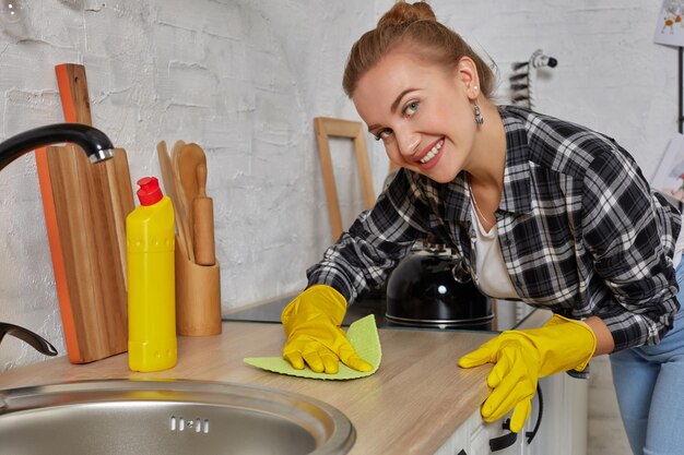 Mulher jovem lavando manualmente, com a mão, usando luvas amarelas de borracha de limpeza.
