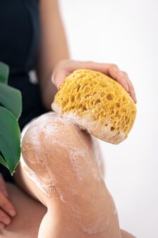 Mulher jovem lavando pernas com esponja amarela e espuma de sabão