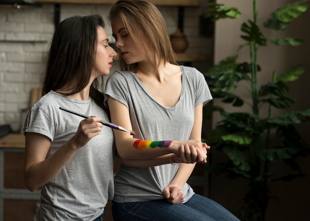 Mulher jovem lésbica pintando bandeira de arco-íris sobre a mão da namorada