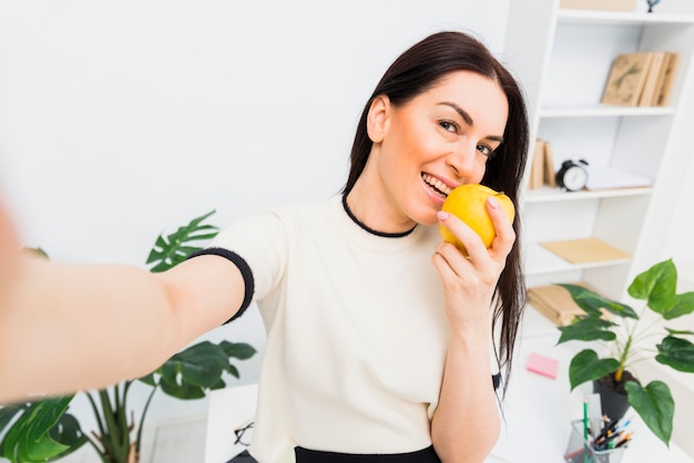 Mulher jovem, levando, selfie, com, maçã, em, escritório