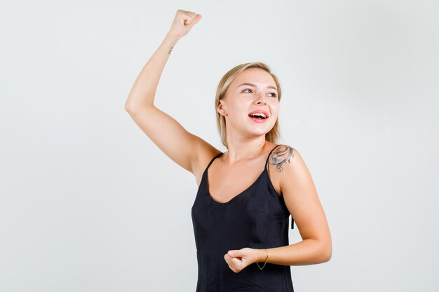Mulher jovem, levantando a mão com o punho cerrado na camiseta preta e parecendo feliz.