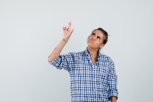 Mulher jovem levantando a mão com os dedos cruzados em uma camisa xadrez