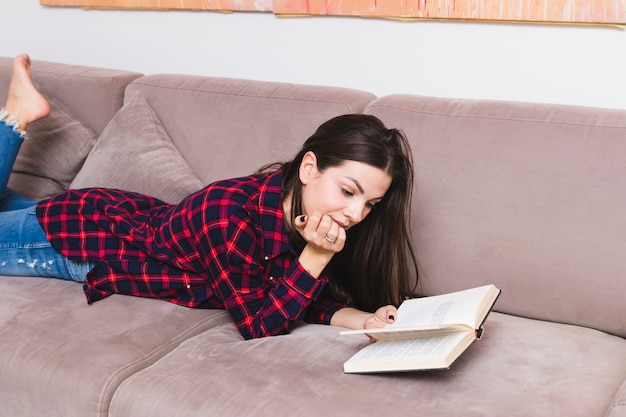 Mulher jovem, mentindo, ligado, sofá, lendo livro