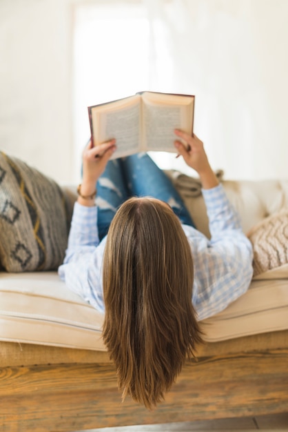 Mulher jovem, mentindo sofá, lendo um livro