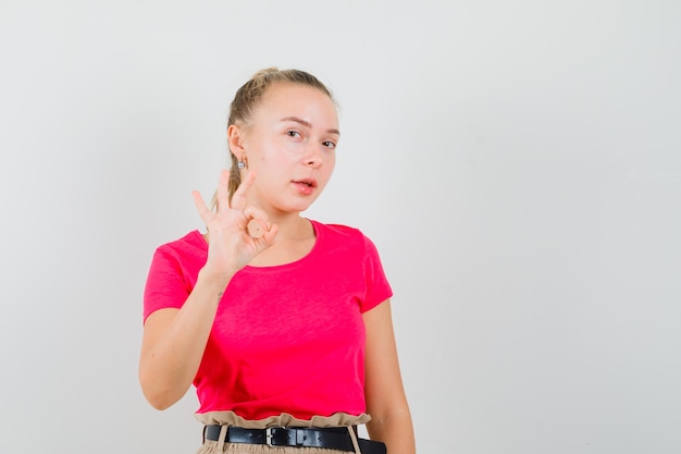 Mulher jovem mostrando gesto de ok com camiseta e calça parecendo confiante