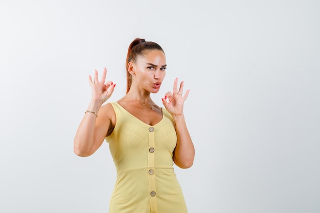 Mulher jovem mostrando gesto de ok em um vestido amarelo e parecendo confiante