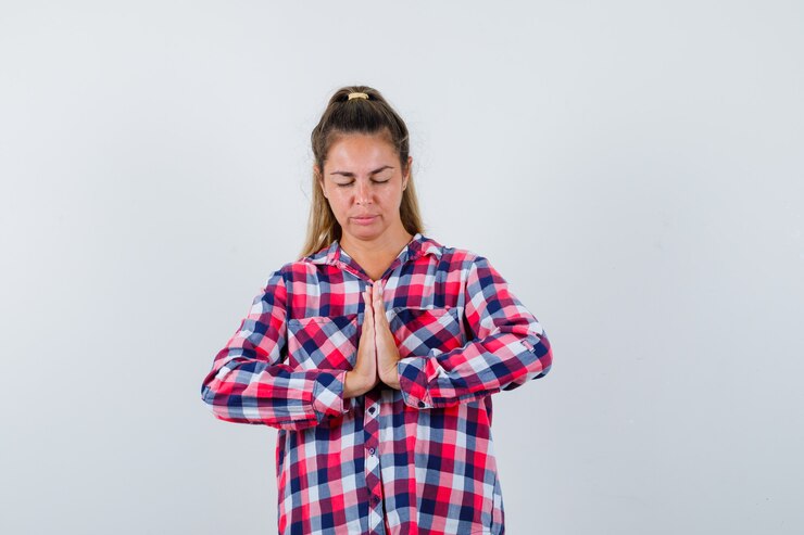 Foto grátis mulher jovem, mostrando o gesto namastê na camisa casual e parecendo esperançosa. vista frontal.