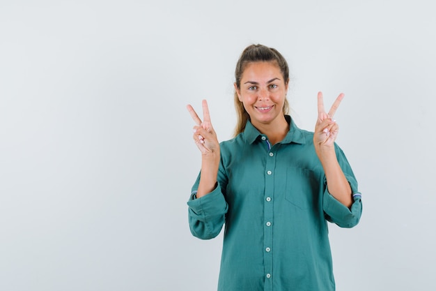 Mulher jovem mostrando o símbolo da paz com as duas mãos na blusa verde e parecendo uma fofa