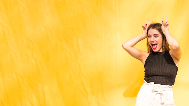 Foto grátis mulher jovem, mostrando, sinal paz, sobre, dela, cabeça, contra, fundo amarelo