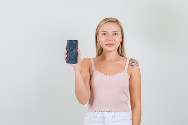 Mulher jovem mostrando smartphone e sorrindo em camiseta