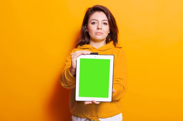 Mulher jovem mostrando tablet com tela verde vertical na câmera