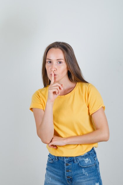 Mulher jovem mostrando um gesto de silêncio em camiseta, shorts e olhando com cuidado