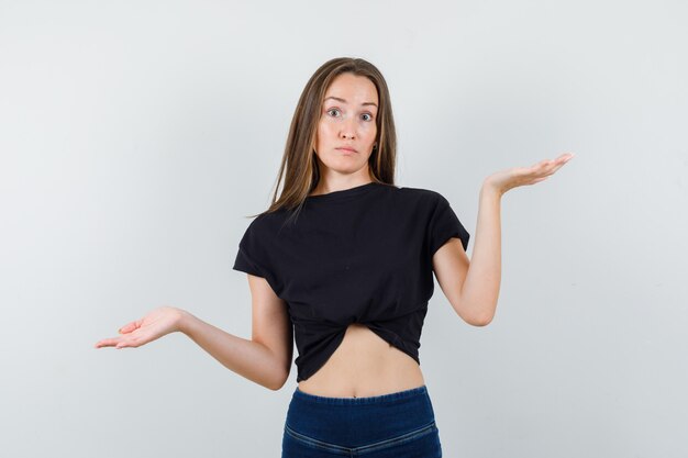 Mulher jovem mostrando um gesto desamparado com uma blusa preta e parecendo triste