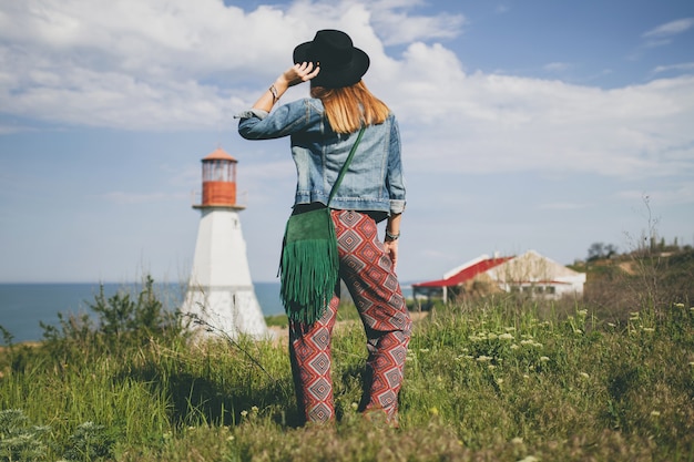 Mulher jovem na natureza, farol, roupa boêmia, jaqueta jeans, chapéu preto, verão, acessórios elegantes