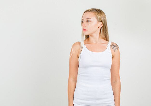 Mulher jovem olhando de lado em uma camiseta branca e parecendo confiante.