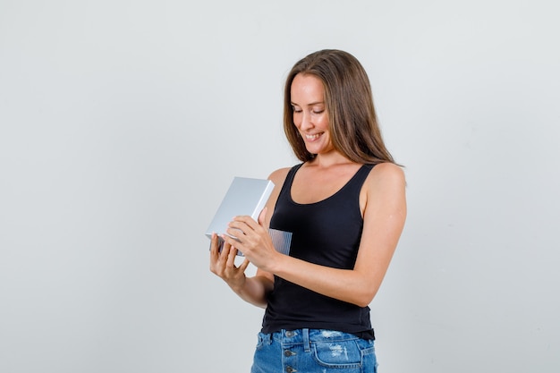 Mulher jovem olhando para uma caixa de presente em camiseta, shorts e parecendo feliz