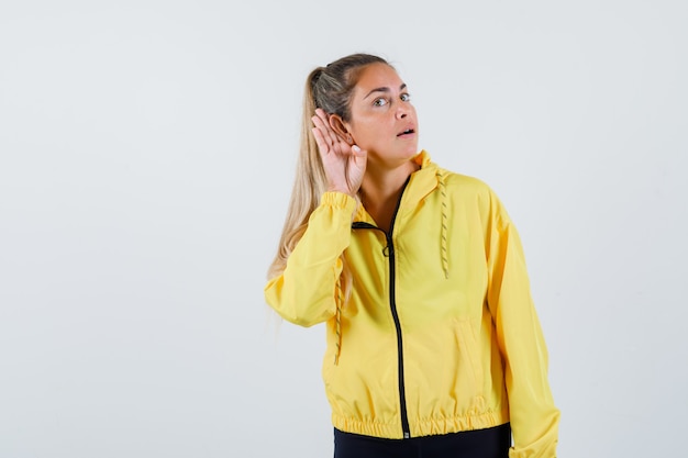 Mulher jovem ouvindo em uma capa de chuva amarela e parecendo concentrada