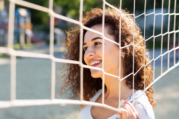 Mulher jovem posando ao lado de um campo de vôlei ao ar livre