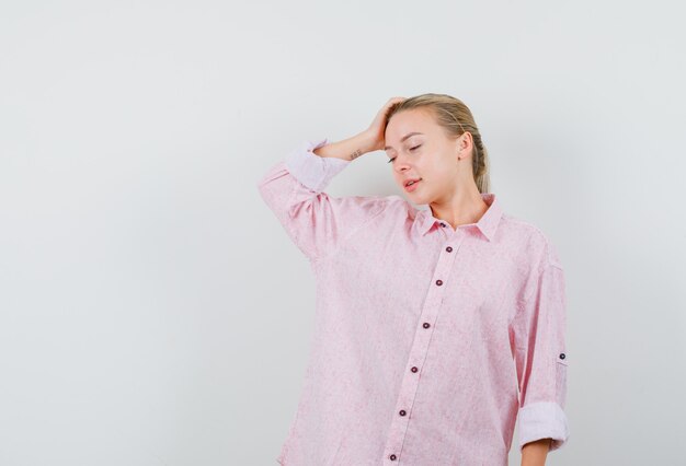 Mulher jovem posando com a mão na cabeça com uma camisa rosa e está muito bonita