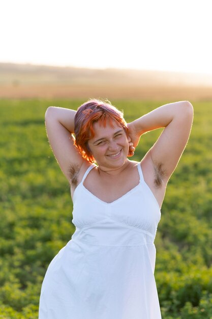Mulher jovem posando com confiança ao ar livre em um campo e mostrando pelos nas axilas