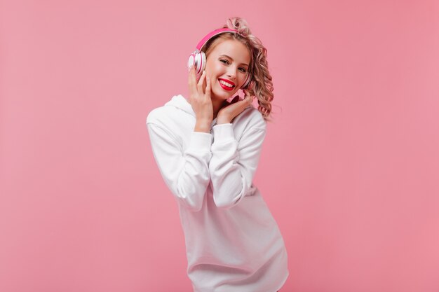 Mulher jovem posando e ouvindo música com seus fones de ouvido cor de rosa