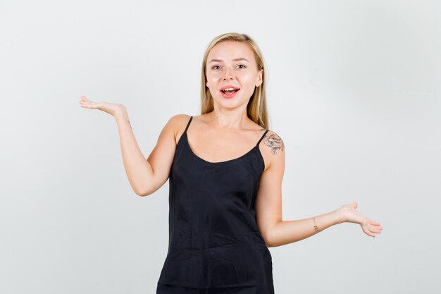 Mulher jovem posando enquanto mostra as palmas das mãos abertas em uma camiseta preta e parecendo alegre