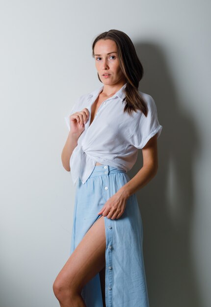 Mulher jovem posando para a frente e colocando a mão na saia em uma camiseta branca e saia azul claro e parecendo encantadora