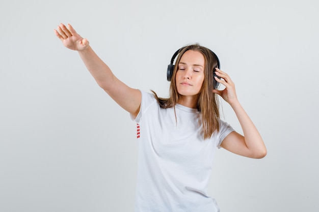 Mulher jovem posando segurando fones de ouvido em uma camiseta branca e parecendo relaxado