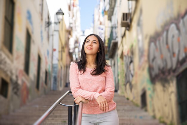 Mulher jovem relaxada, apoiando-se na grade de escadas da cidade