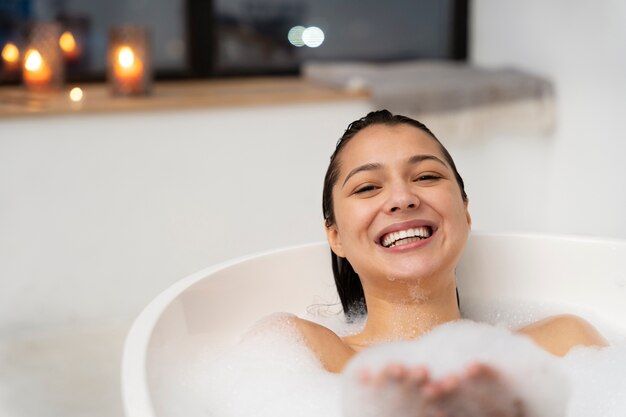 Mulher jovem relaxando e brincando com espuma enquanto toma banho