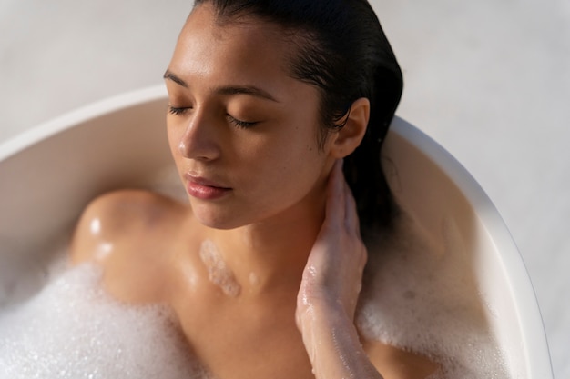 Mulher jovem relaxando e tomando banho em uma banheira cheia de água e espuma