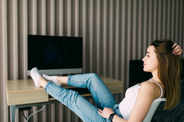 Mulher jovem relaxando em casa, sentada com os pés descalços sobre uma mesa e os olhos fechados