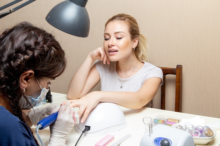 Foto grátis mulher jovem reparando as unhas pela manicure dentro do quarto beleza manicure unhas mão senhora autocuidada