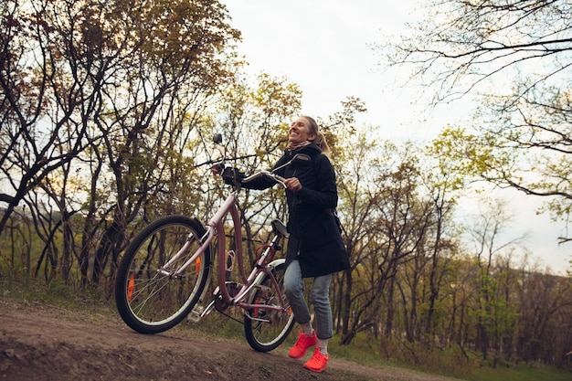 Mulher jovem se divertindo perto do parque rural, andando de bicicleta, viajando na primavera