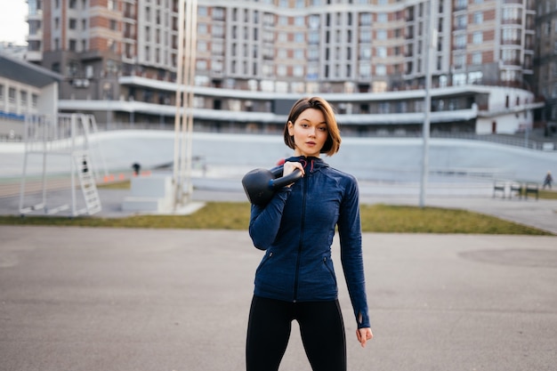 Mulher jovem se exercitando com um kettlebell do lado de fora no estádio