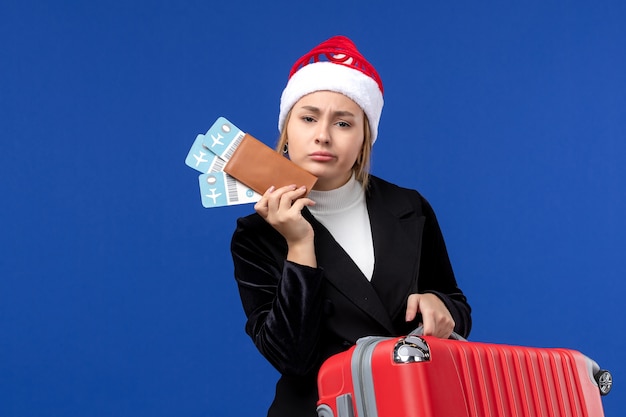 Mulher jovem segurando a bolsa de frente e ingressos para as férias de férias de avião de parede azul