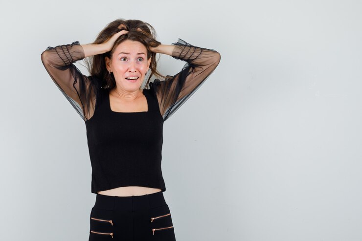 Foto grátis mulher jovem segurando a cabeça com as mãos na blusa preta e parecendo ansiosa. vista frontal. espaço para texto